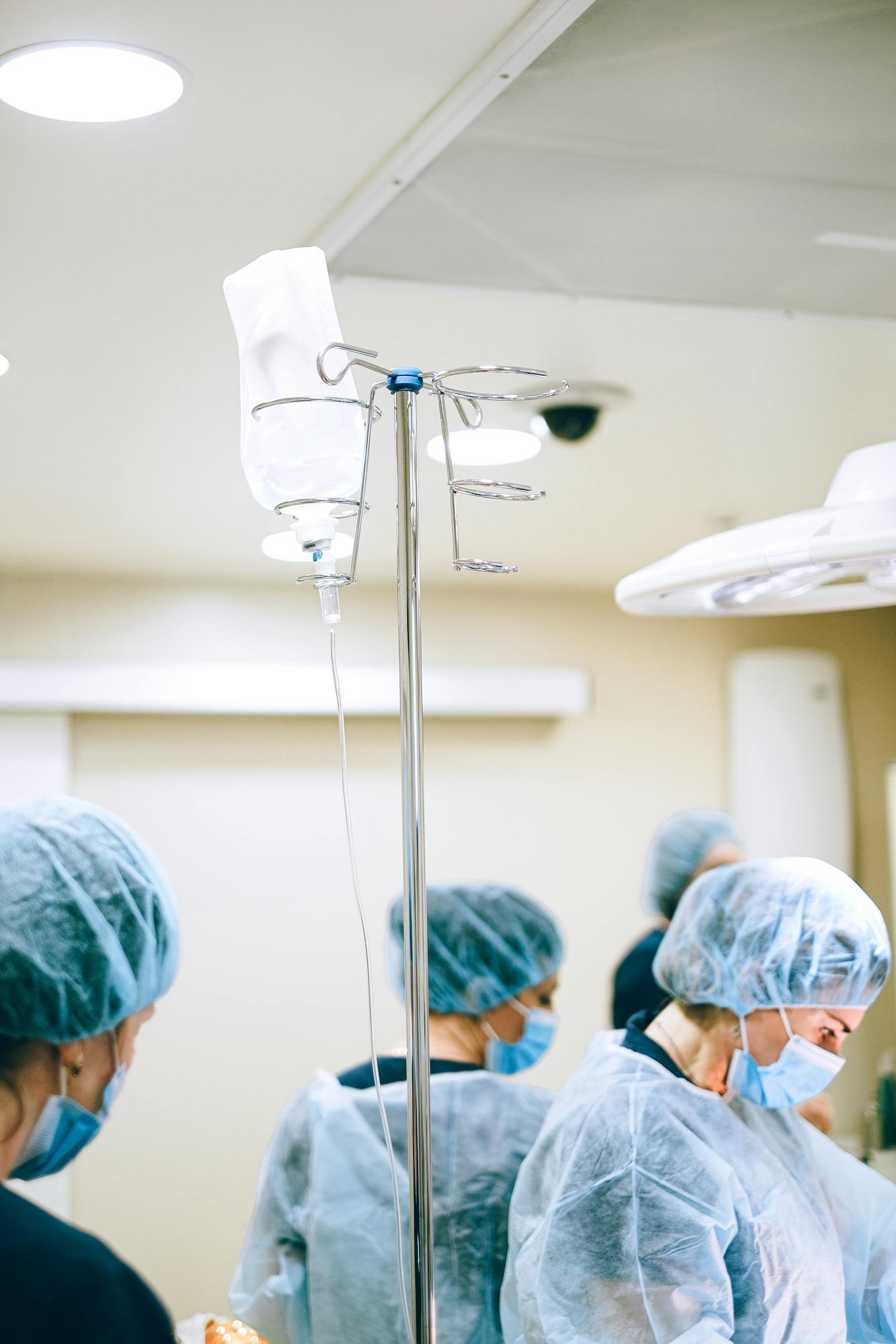 A Dextrose on a Pole Near People Wearing a Personal Protective Equipment in a Room