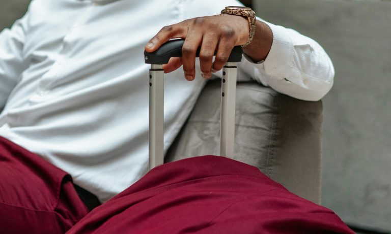 Close-up of a business traveler's hand resting on a suitcase handle, dressed in casual attire.