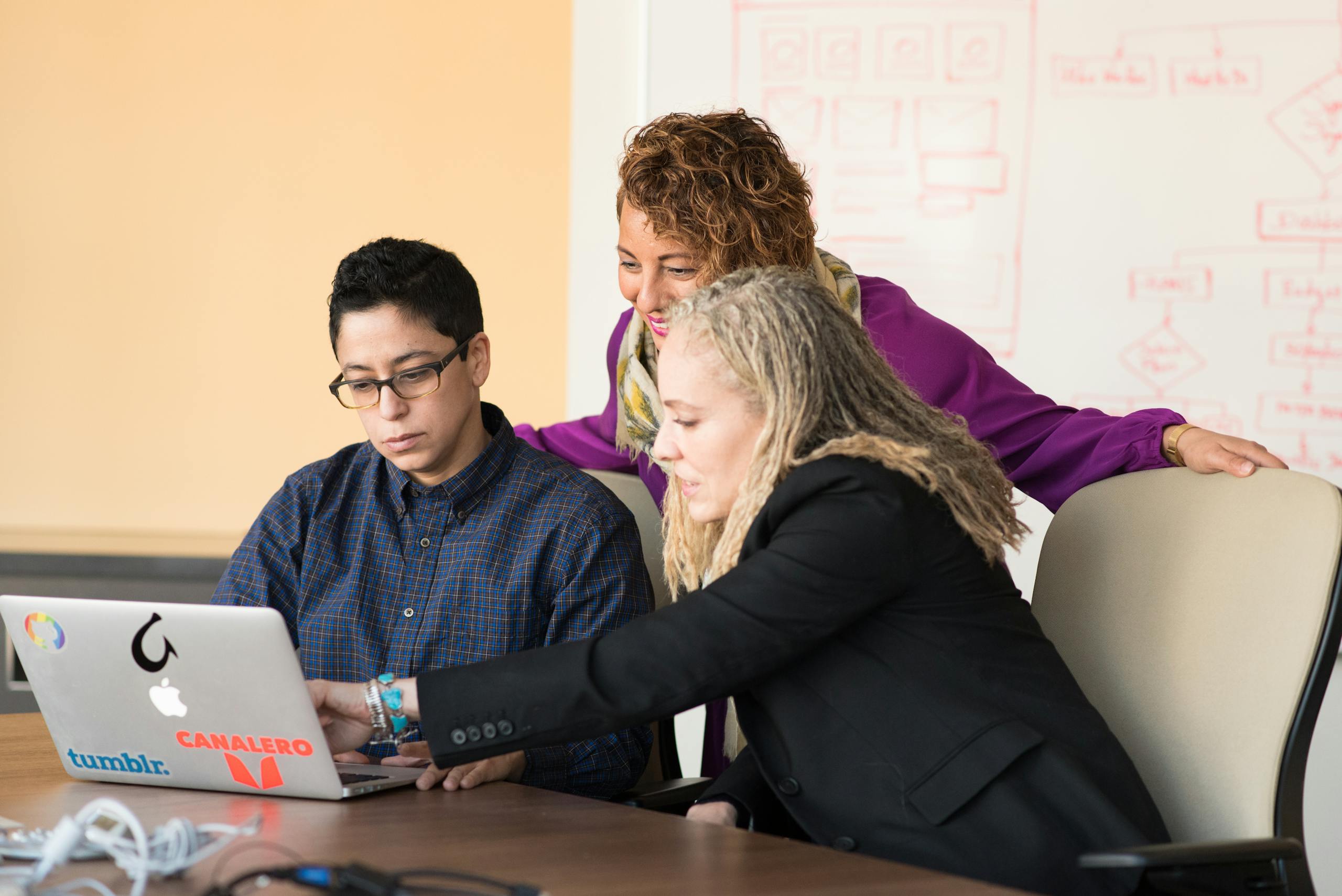 Three colleagues collaborating on a laptop in a tech-focused office environment.