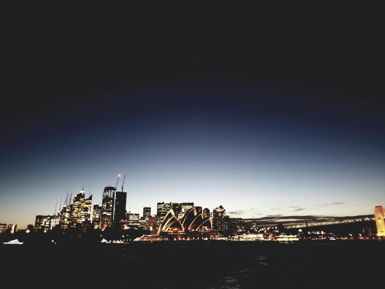 Iconic view of Sydney Opera House and city skyline during twilight, captured with a dramatic silhouette.