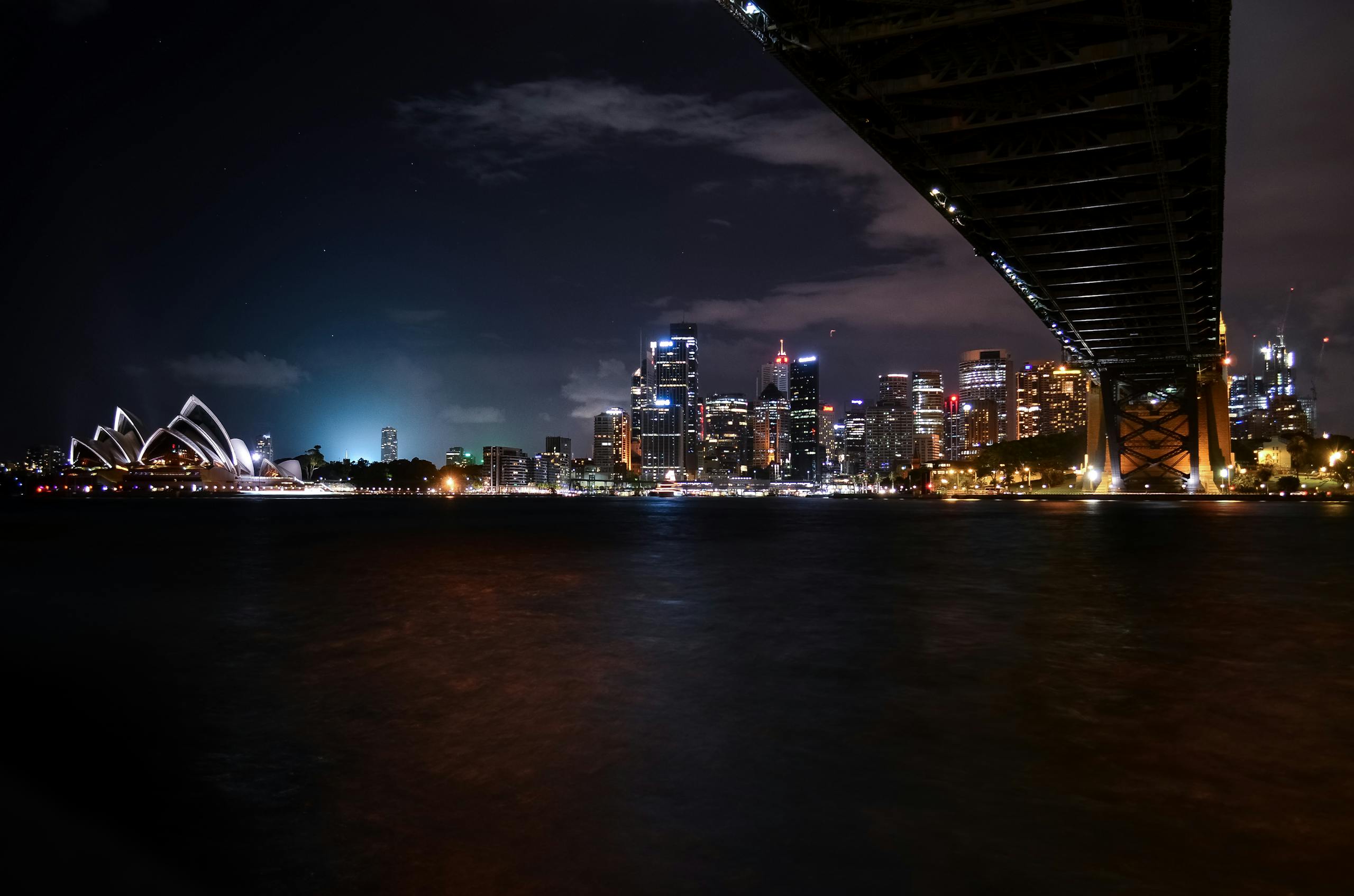 Scenic nighttime view of Sydney Opera House and city skyline under Harbour Bridge.